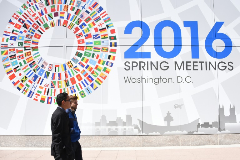 Deux hommes passent devant un panneau annonçant le meeting du monde de la finance à Washington, le 13 avril 2016. © AFP